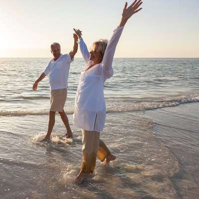 A happy couple walks hand in hand on the beach with arms raised in joy after couples counseling online